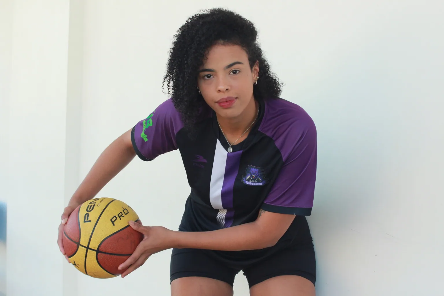 Carol, atleta da Atlética Humanas da UFU, posa com uma bola de basquete usando o uniforme roxo da equipe.